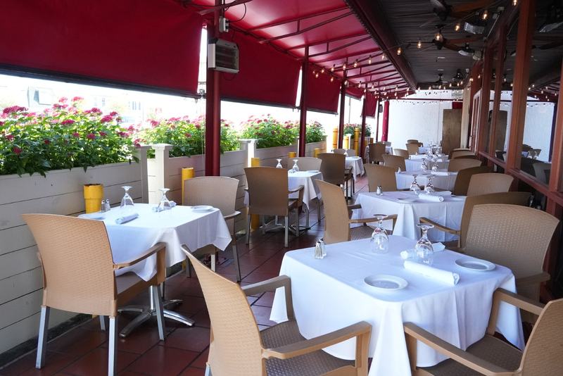 The covered patio at Casa Mia Trattoria in North Miami, with white tablecloths, red awnings, and flowering planters
